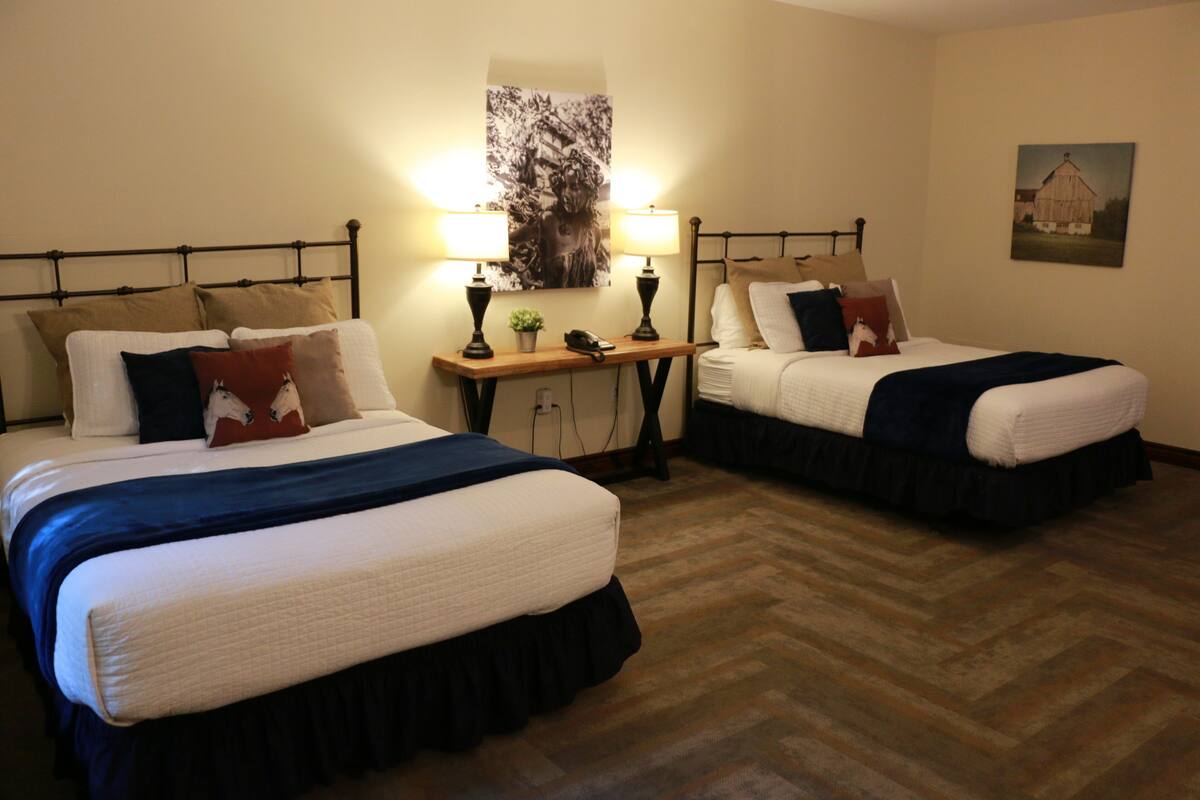 A hotel room with two beds, each with a headboard, bedside tables with lamps, and a large framed picture on the wall.
