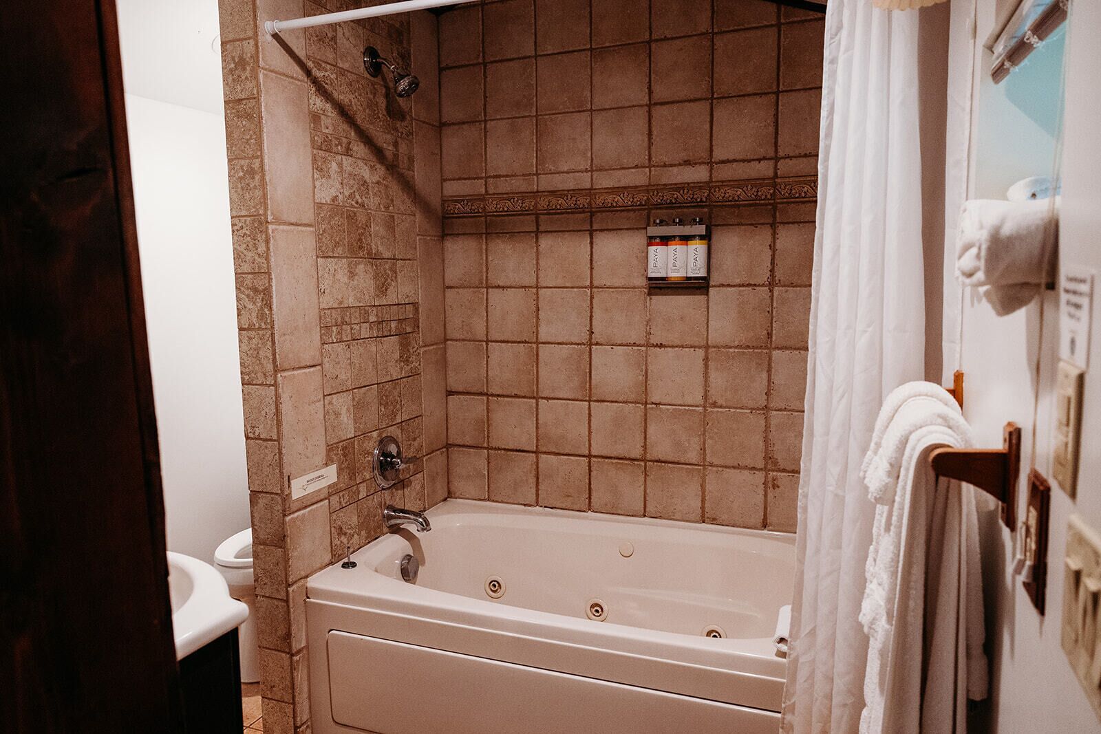 A bathroom with a bathtub, a shower, and a toilet. There are towels hanging on a rack and a shelf with toiletries.