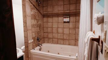 A bathroom with a bathtub, a shower, and a toilet. There are towels hanging on a rack and a shelf with toiletries.