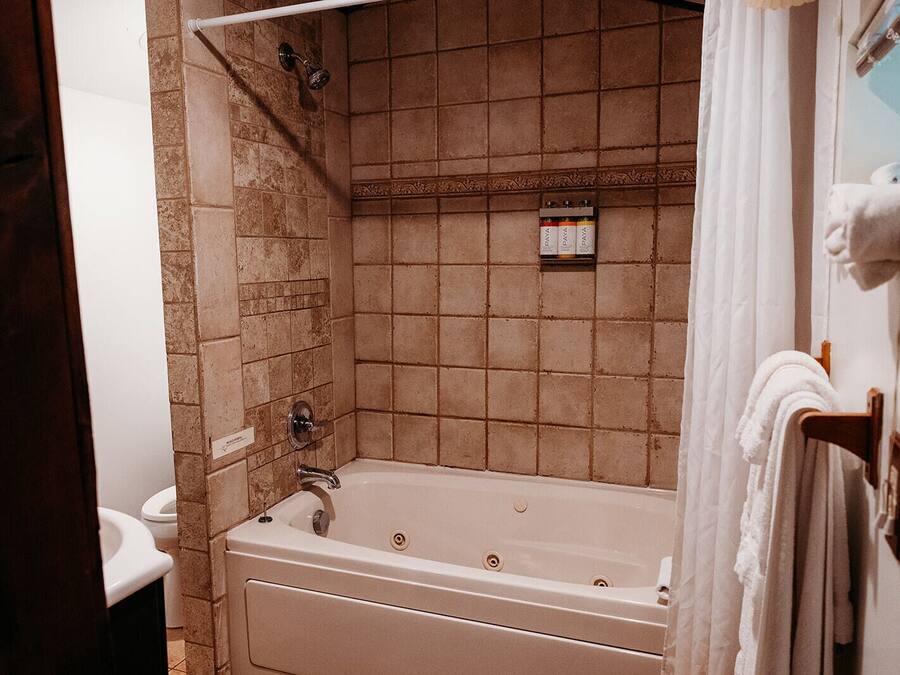 A bathroom with a bathtub, a shower, and a toilet. There are towels hanging on a rack and a shelf with toiletries.