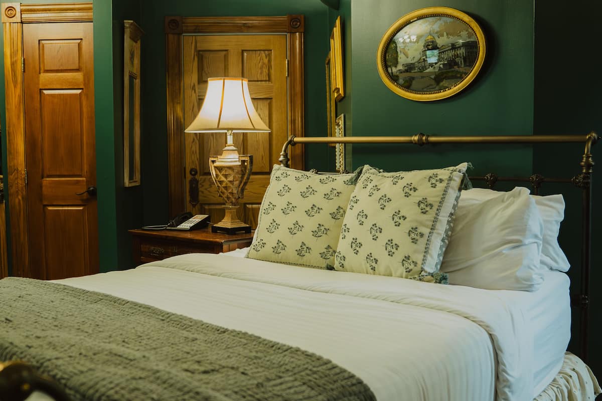 A neatly made bed with floral pillows, a bedside lamp, and a wooden nightstand with a telephone.
