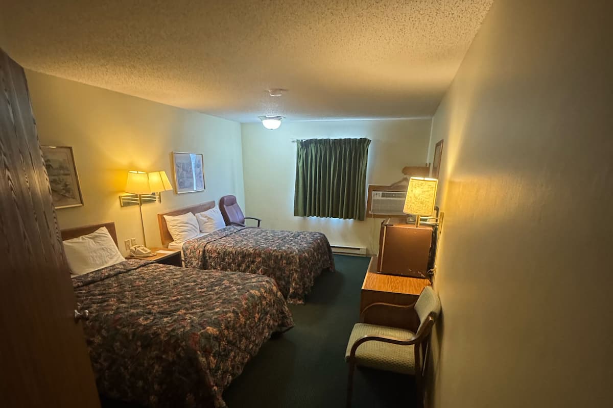 A hotel room with two beds, a desk, a chair, a lamp, and a trash bin.