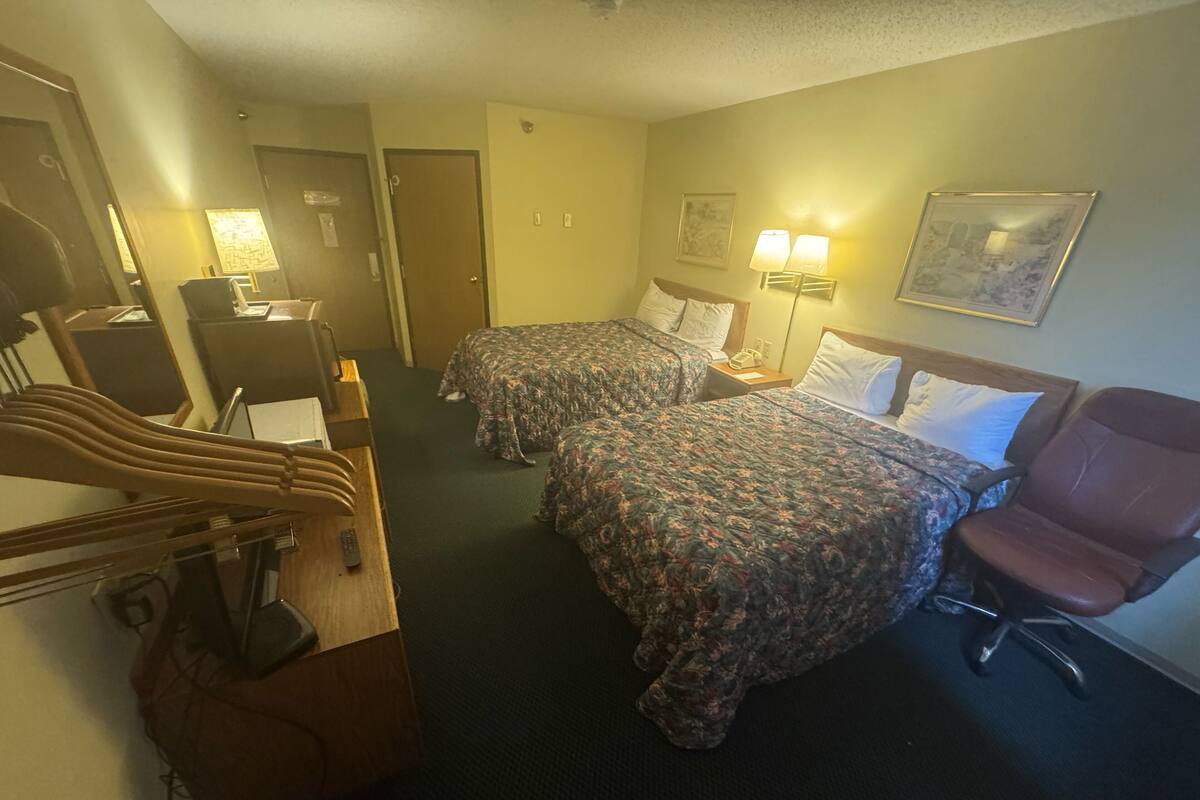 A hotel room with two beds, a desk with a telephone, a chair, and a lamp.