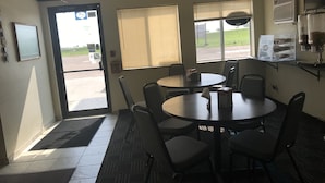 Una habitación con una mesa redonda, cuatro sillas, una ventana con persianas, una puerta y un aire acondicionado de pared.
