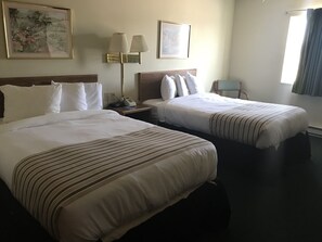 A hotel room with two beds, a nightstand with a lamp, and a chair.