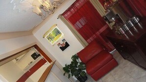 A living room with a red sofa, a potted plant, and a kitchen area with cabinets and a stove. - Sherkston Inn (Port Colborne)