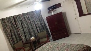 A bedroom with a bed, a wardrobe, a chair, a small table, and a ceiling fan. - Sherkston Inn (Port Colborne)