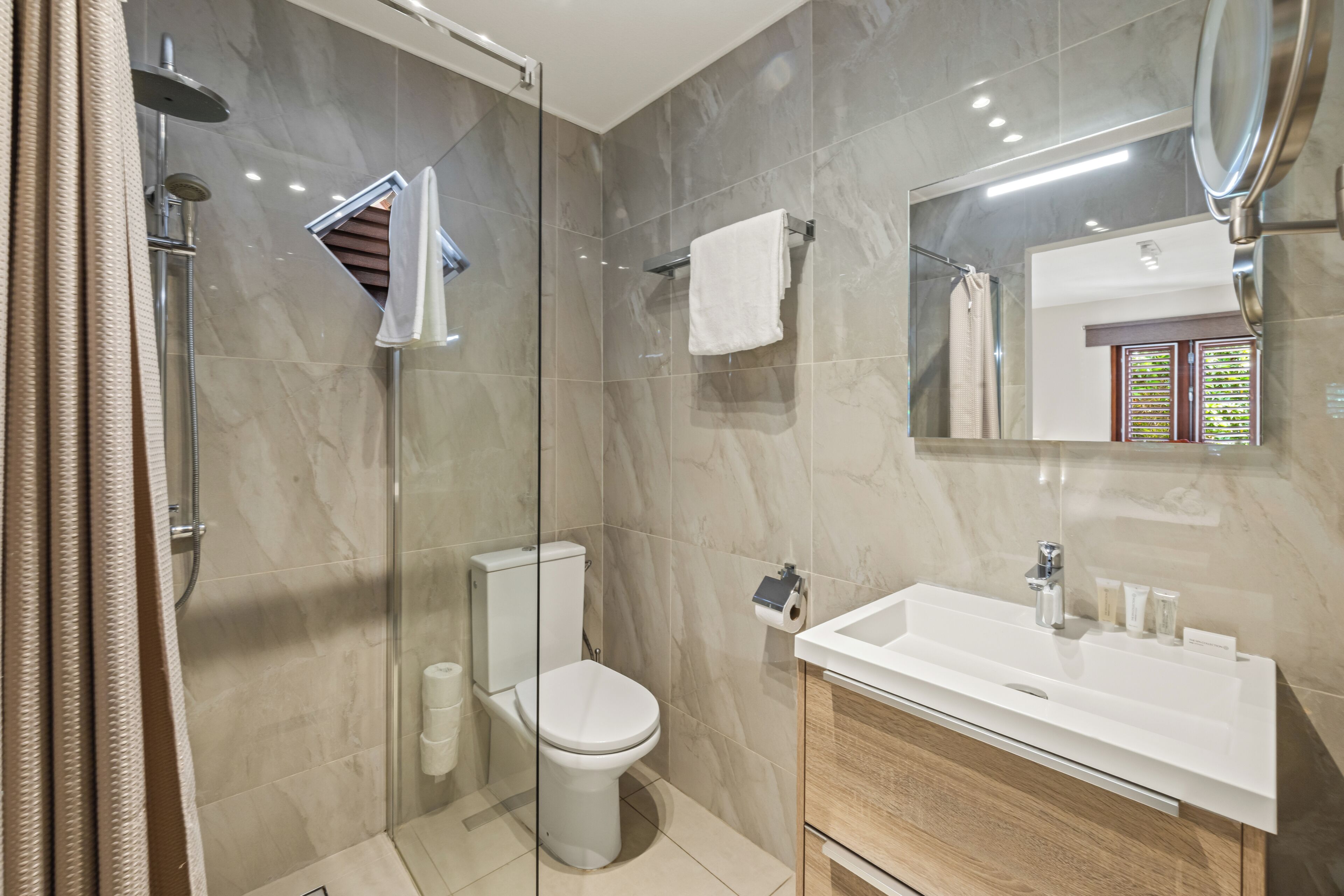 Un baño moderno con ducha envuelta en vidrio, inodoro blanco, lavamanos con espejo y barra para toallas.