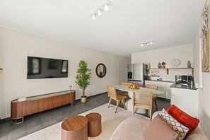 A modern living room with a flat-screen TV, a dining area, and a kitchen.