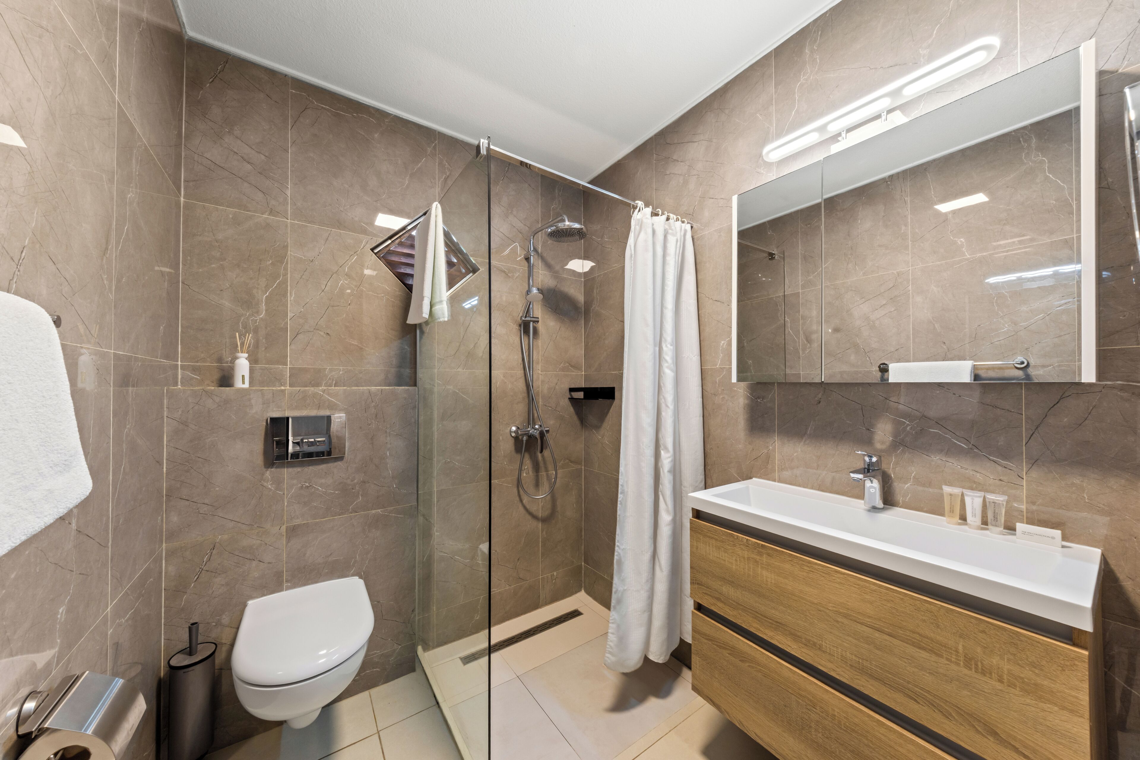Un baño moderno con ducha envuelta en vidrio, inodoro y tocador con espejo.