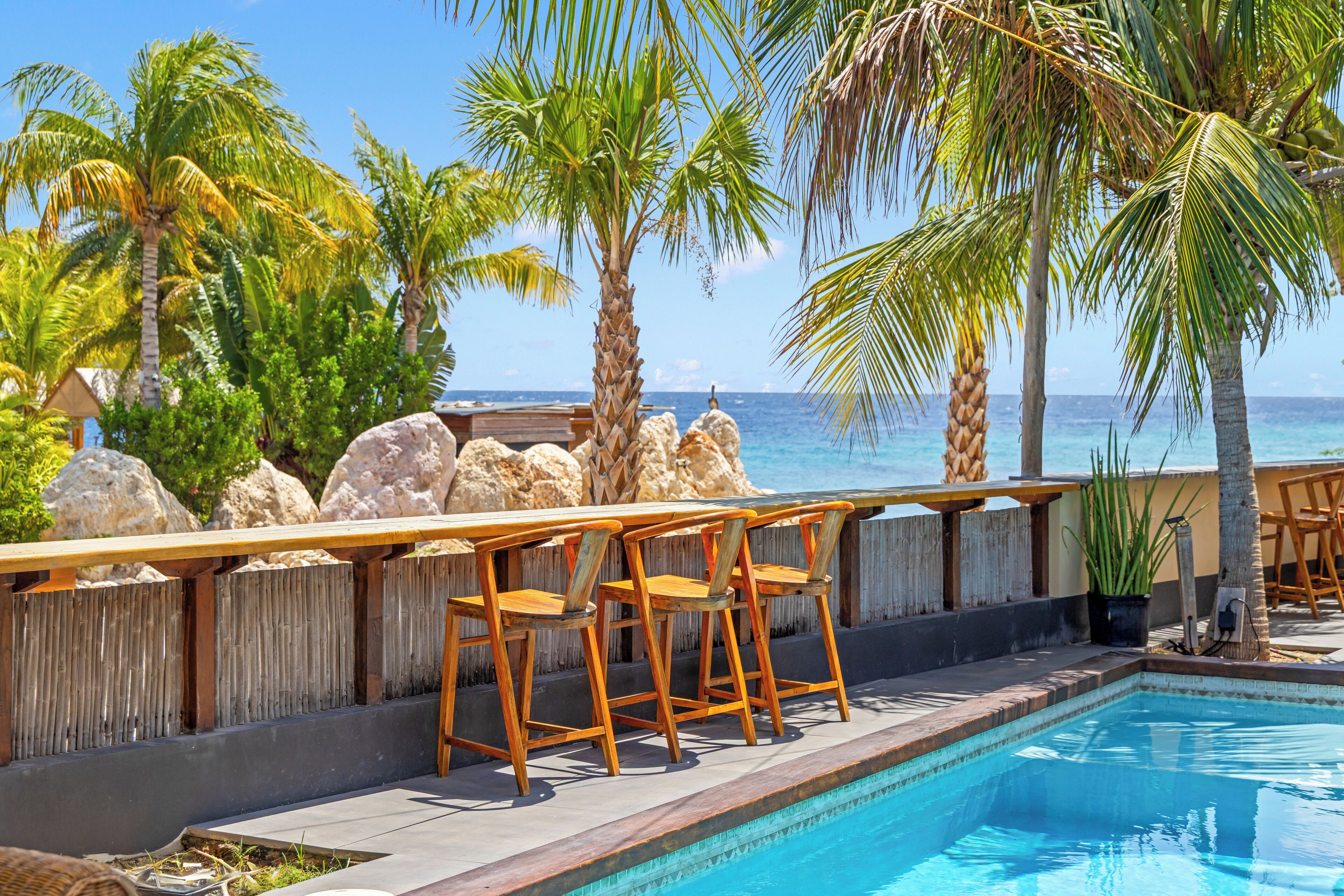 Un espace aménagé au bord de la piscine, avec des chaises en bois, une terrasse en bois et une vue sur l’océan.