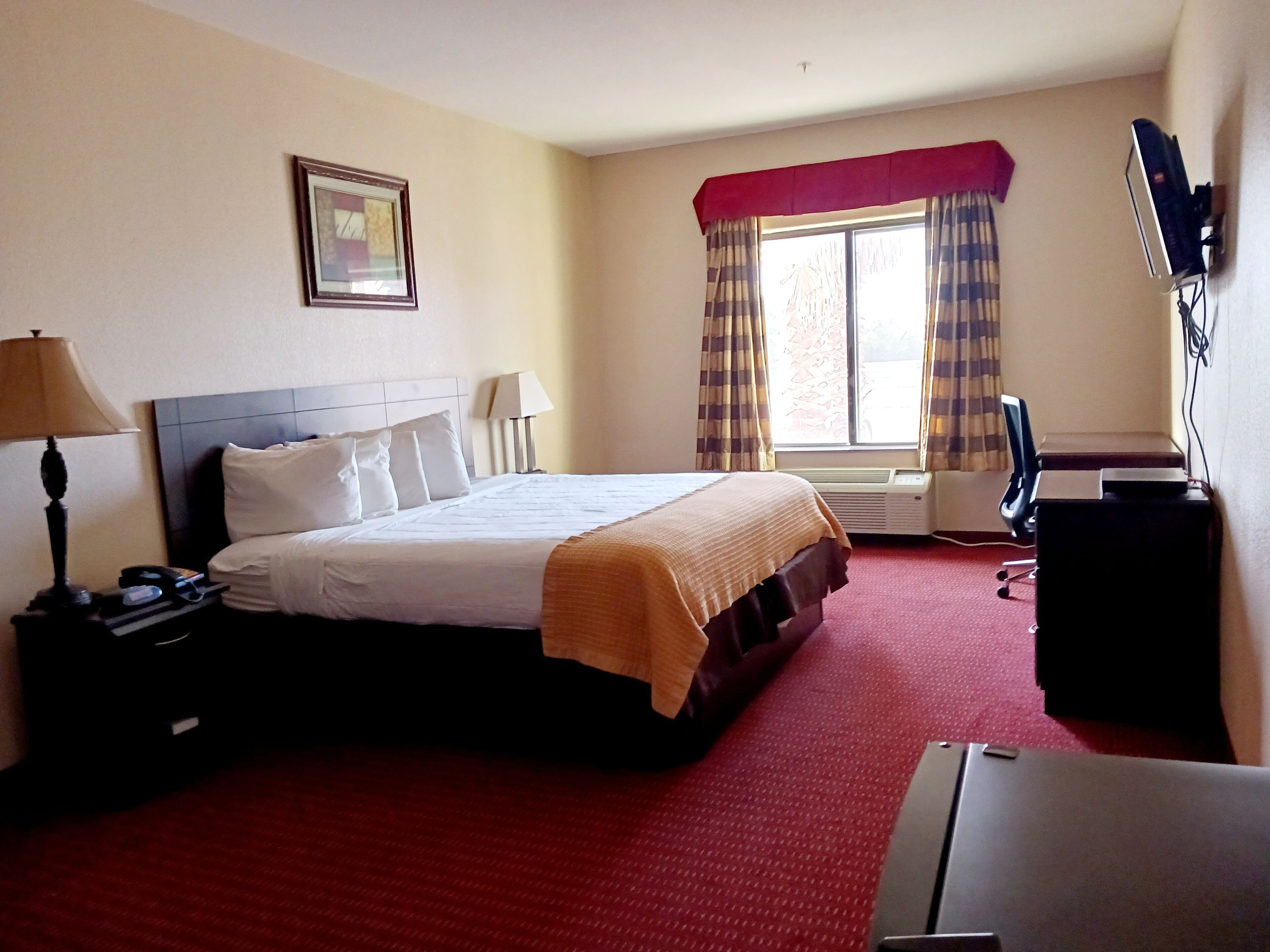 A hotel room with a bed, a desk, a chair, a TV, and a window with curtains.