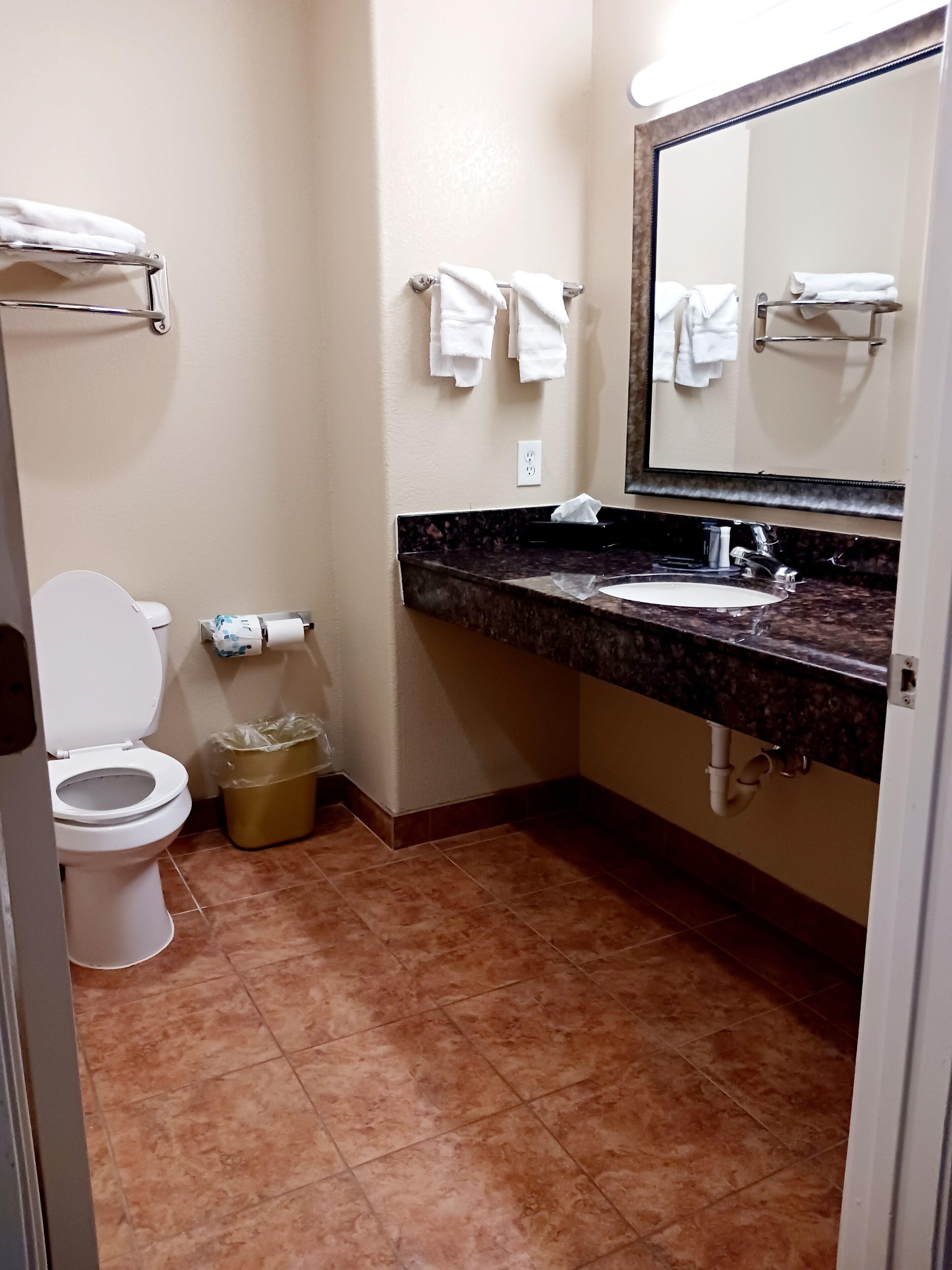 Une salle de bain équipée de toilettes, d’un lavabo, d’un miroir et de serviettes accrochées à des crochets.