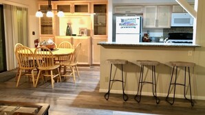 A kitchen with wooden cabinets, a refrigerator, a microwave, and a bar area with stools. - Escape For All Seasons (Big Bear Lake)