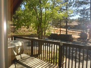 A wooden deck with a table and chairs, overlooking a landscaped area with trees and a paved path.