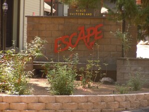 A brick wall with the word "ESCAPE" in large red letters, a sign indicating address 41935 SWITZERLAND, and some greenery in front.