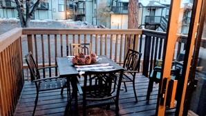 A wooden deck with a table and chairs, a bowl of pinecones, and a view of houses in the background. - Escape For All Seasons (Big Bear Lake)