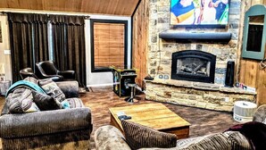 A cozy living room with a stone fireplace, comfortable seating, and a television mounted on the wall. - Escape For All Seasons (Big Bear Lake)
