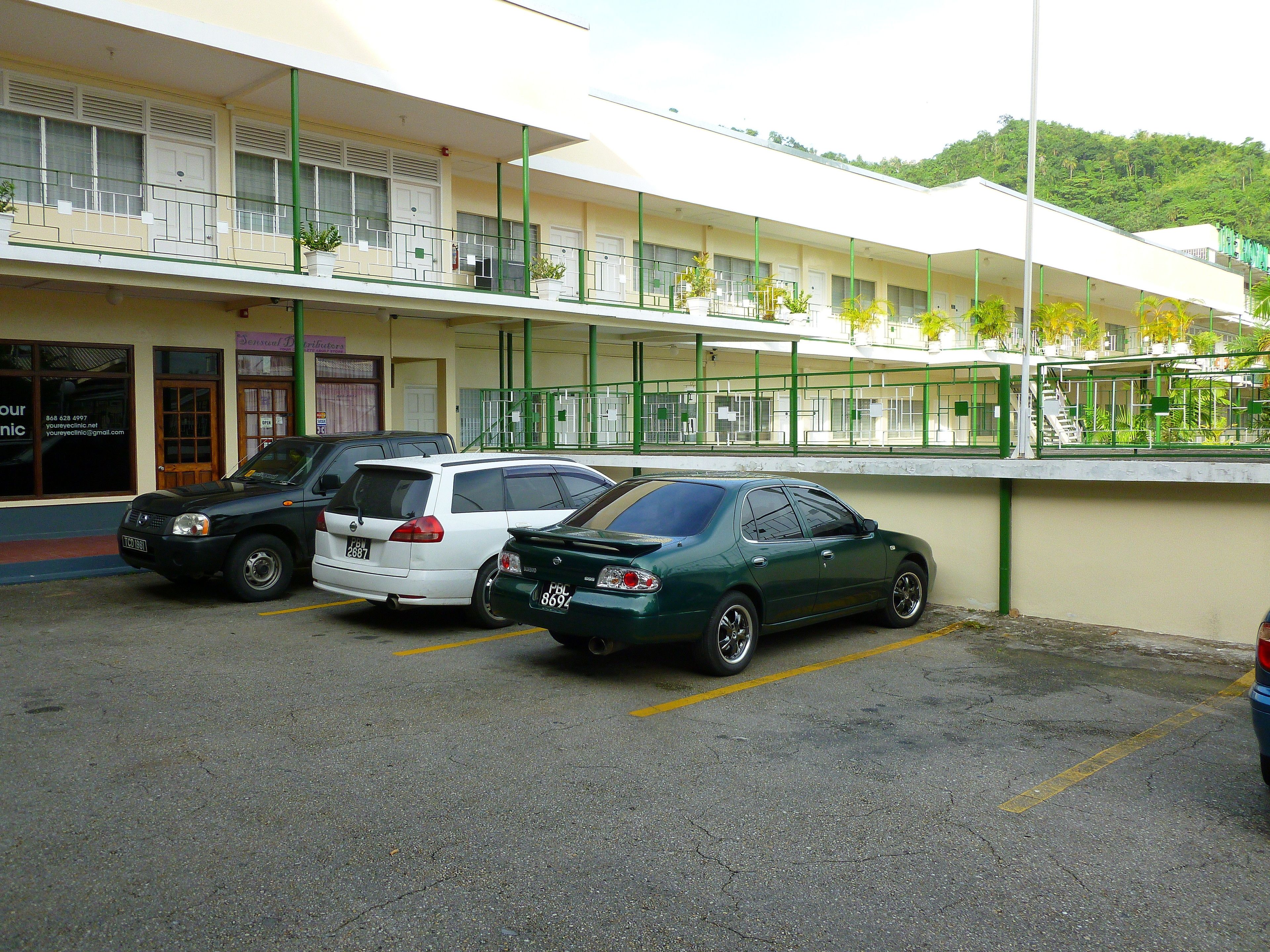 Un parking où sont garées trois voitures devant un immeuble à étages, doté de balcons.