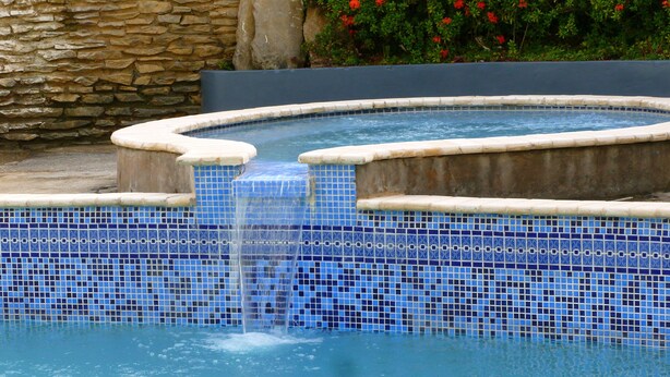 A swimming pool with a blue mosaic tile border and a stone wall in the background. - Royal Palm Suite Hotel (Port of Spain)