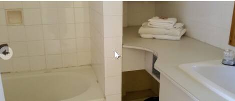 A bathroom with a bathtub, a sink, and a stack of folded towels.