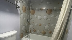 Une salle de bain avec des toilettes, une baignoire dotée d’un rideau de douche et un mur orné de motifs circulaires.