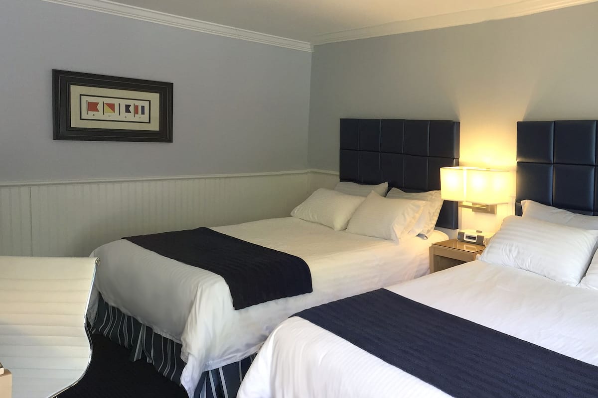 A hotel room with two beds, a nightstand with a lamp, and a framed picture on the wall.