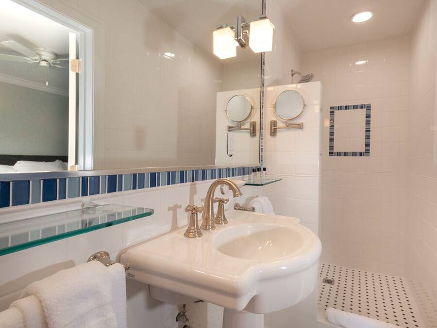 A bathroom with a white sink, two mirrors, and a glass shelf.