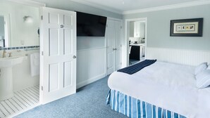 A bedroom with a bed, a white door, a bathroom with a sink, and a ceiling fan. - Atlantic Inn (Wethersfield)