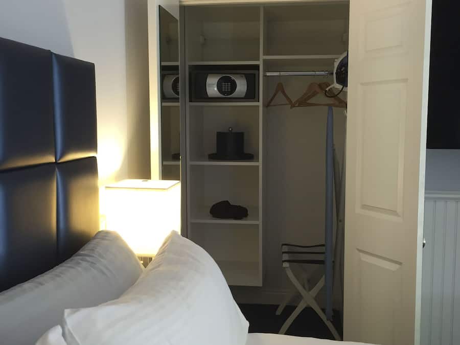 Habitación de hotel con cama, lámpara de noche, armario y abrigo colgado en la puerta.