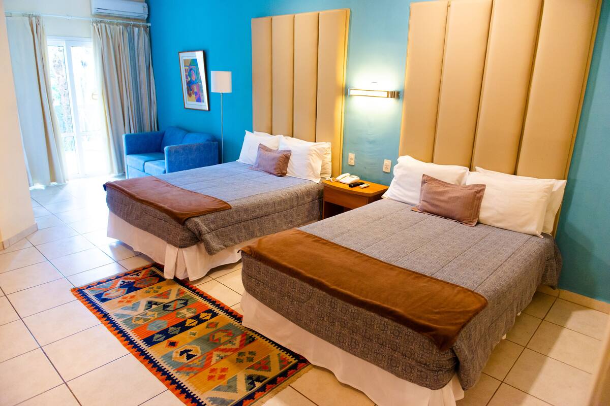 Habitación de hotel con dos camas, una pared azul, una alfombra estampada y una mesita de noche con un teléfono.