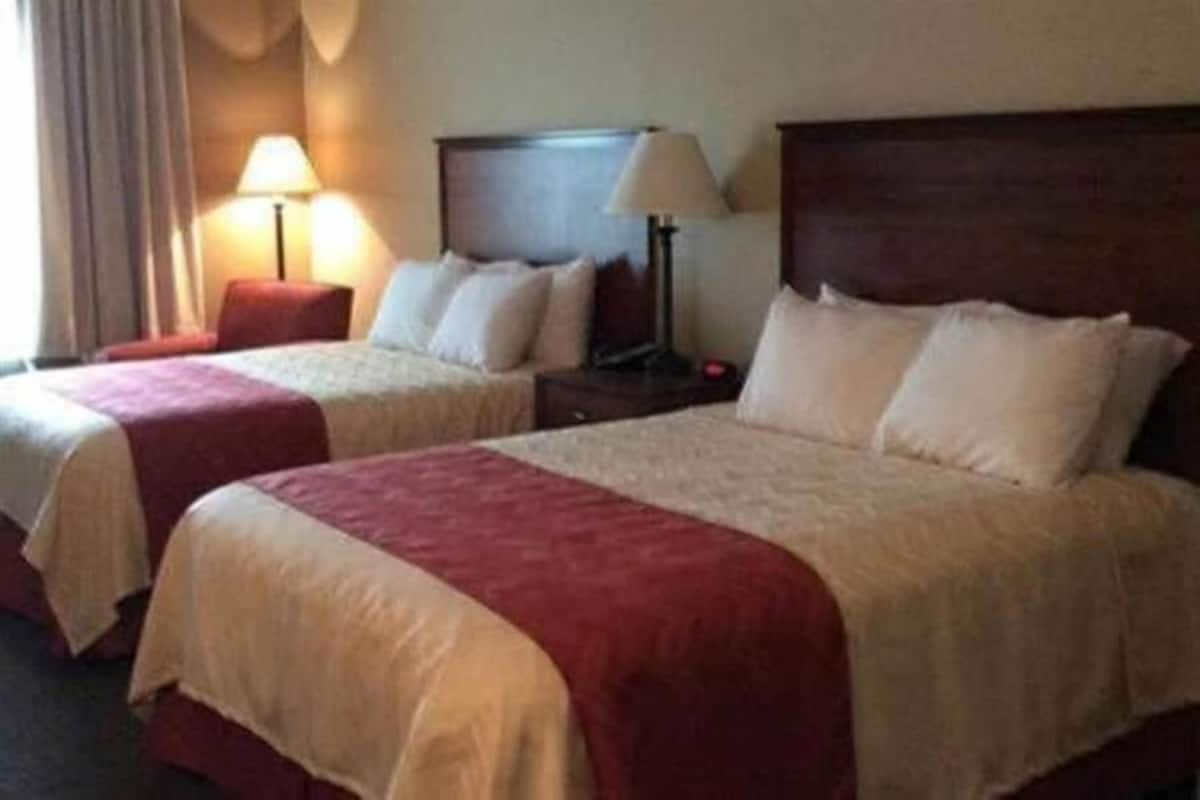 A hotel room with two beds, each with a red and white bedspread, a wooden headboard, and bedside lamps.