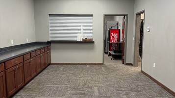 A spacious, carpeted room with a long counter and wooden cabinets, a window with blinds, and a door leading to another area.