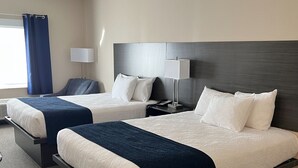 A hotel room with two beds, a dark headboard, a bedside table with a lamp, and a window with curtains.