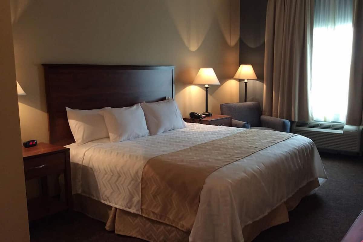 A hotel room with a large bed, two bedside lamps, a chair, a nightstand, and a window with curtains.