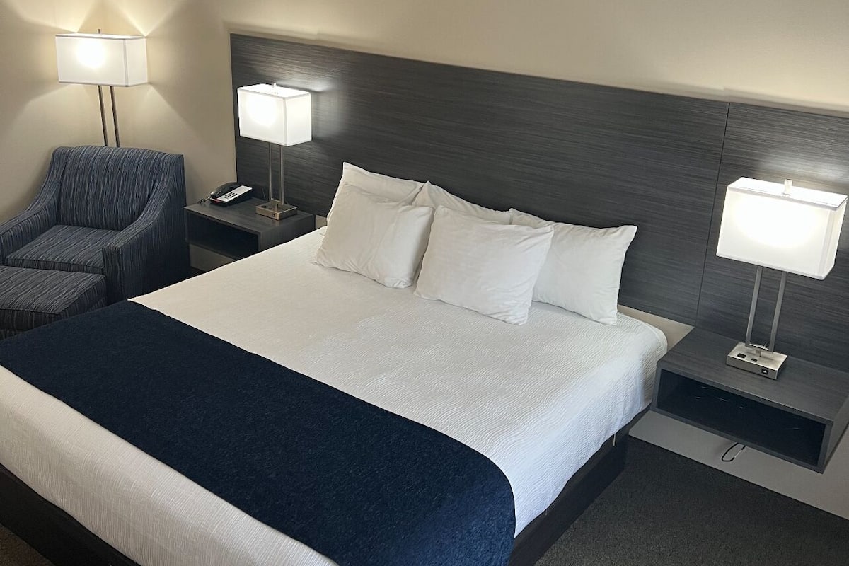 A hotel room with a large bed, two bedside tables, a chair, and two lamps.