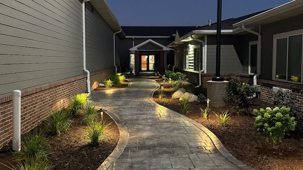 A paved pathway leading to a building with a dark exterior and a lighted entrance.