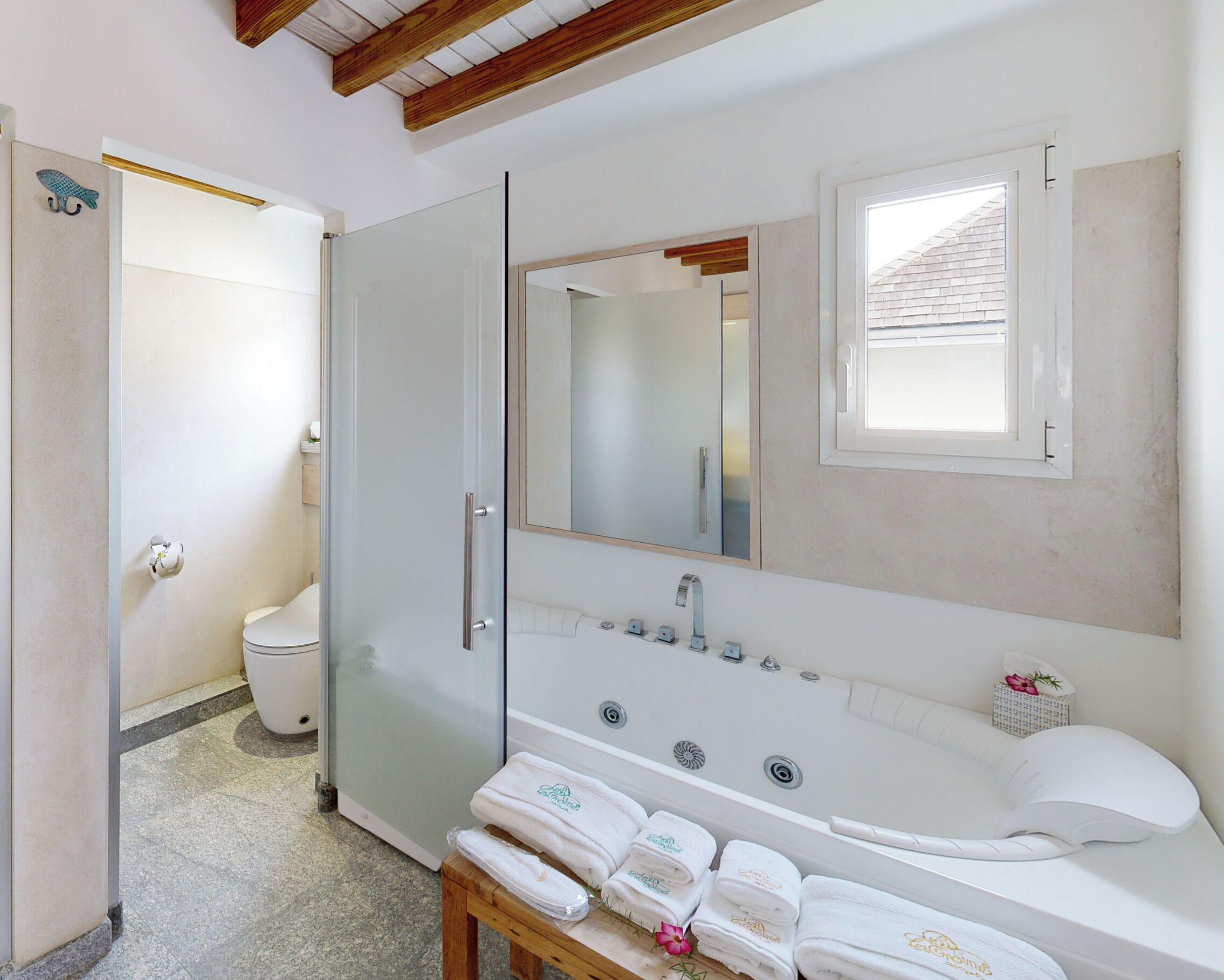 Une salle de bain moderne avec une douche à parois de verre, un grand miroir, une baignoire et des serviettes soigneusement pliées sur un tabouret en bois.