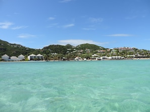 A coastal resort with overwater bungalows, clear turquoise water, and lush green hills in the background.