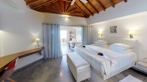 Habitación de hotel con una cama grande, un escritorio con lámpara, techo de madera y vista al pasillo.