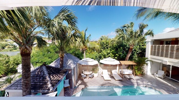 A pool area with lounge chairs and umbrellas, surrounded by palm trees and a view of a body of water. - Hotel Les Ondines Sur La Plage (St. Barthelemy)