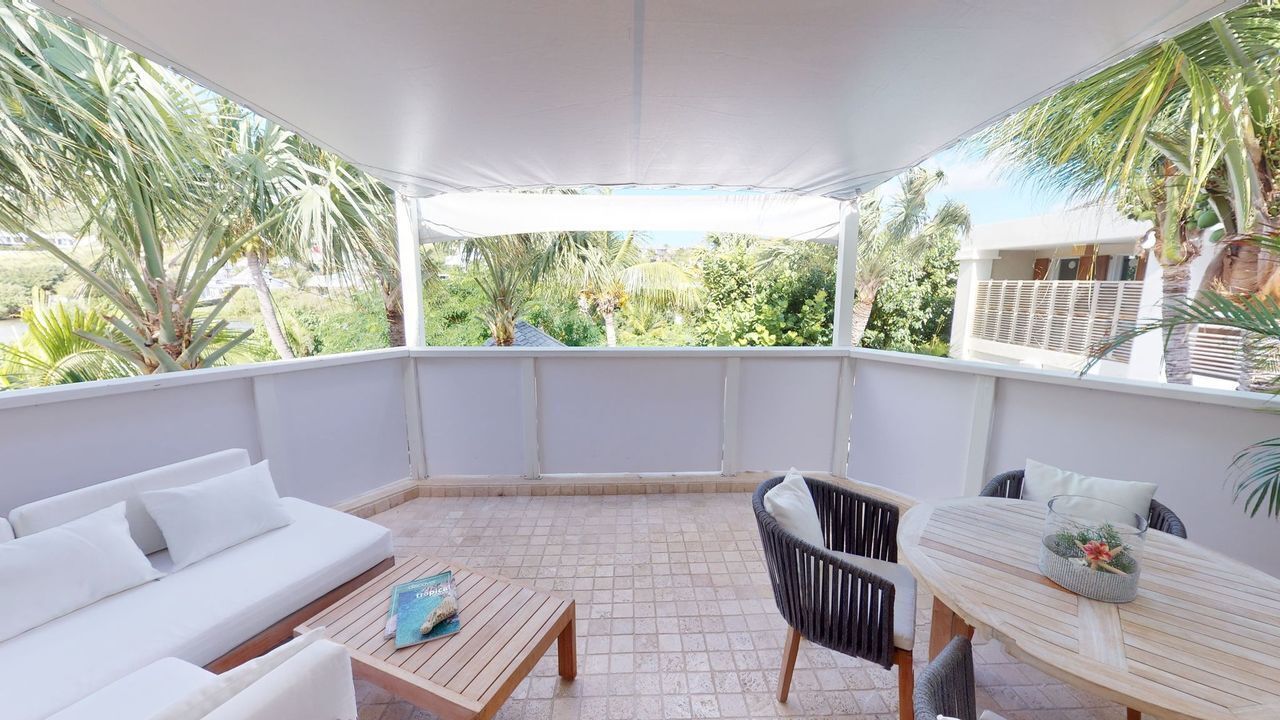 Een overdekte terras met een witte bank, een houten tafel en een rieten stoel.