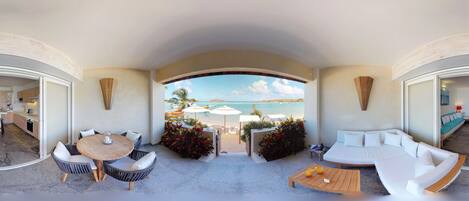 A modern interior with a curved ceiling, a round dining table, a sofa, and a view of a beach with umbrellas.