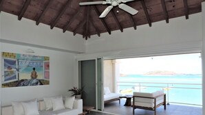 Un salón espacioso con un sofá blanco, una mesa de centro de madera con libros, y un cuadro en la pared.