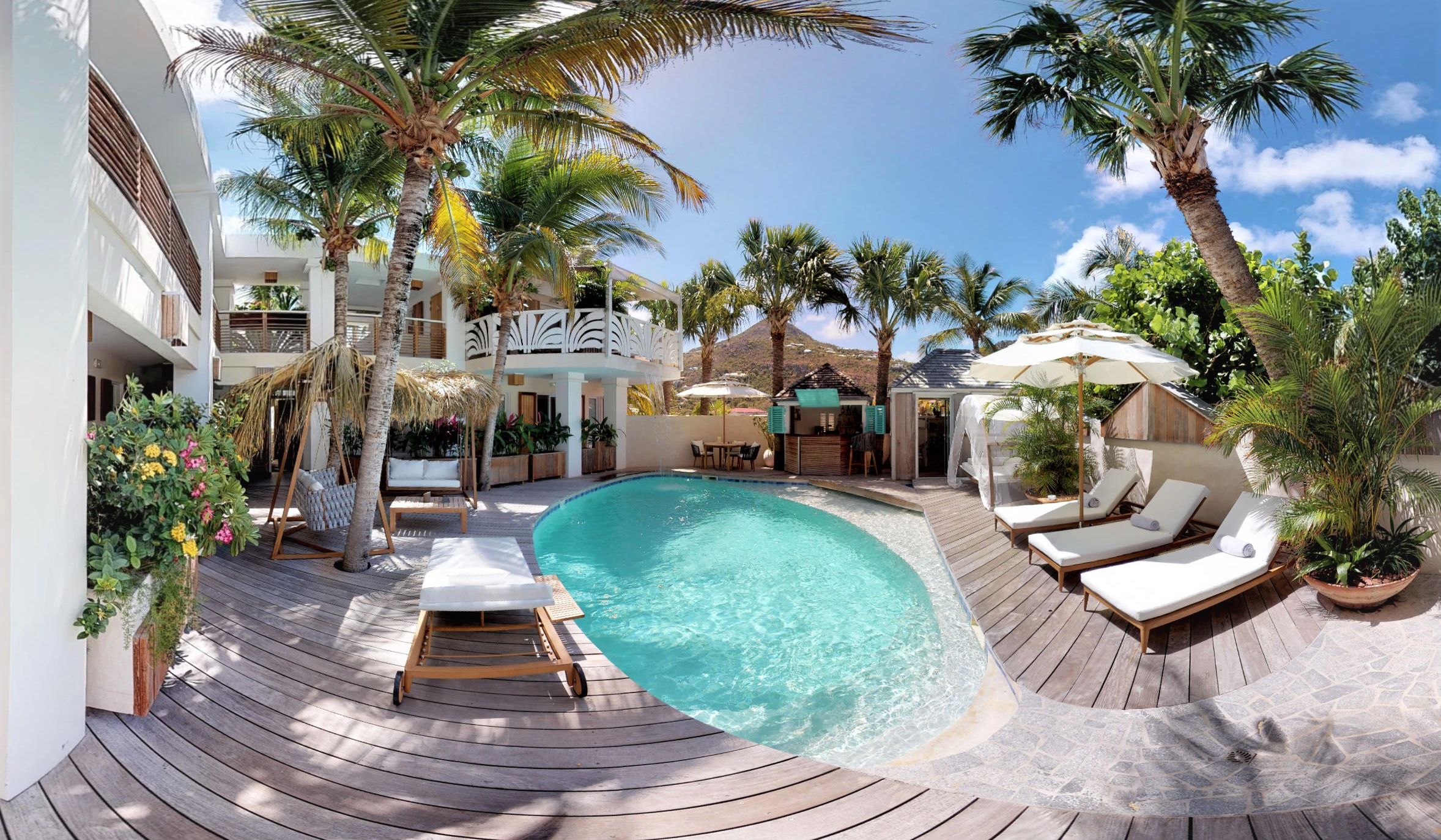 A pool area with lounge chairs, a wooden deck, and palm trees.