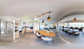 A modern kitchen with a central island, stainless steel appliances, and a dining area with a wooden table and wicker chairs.