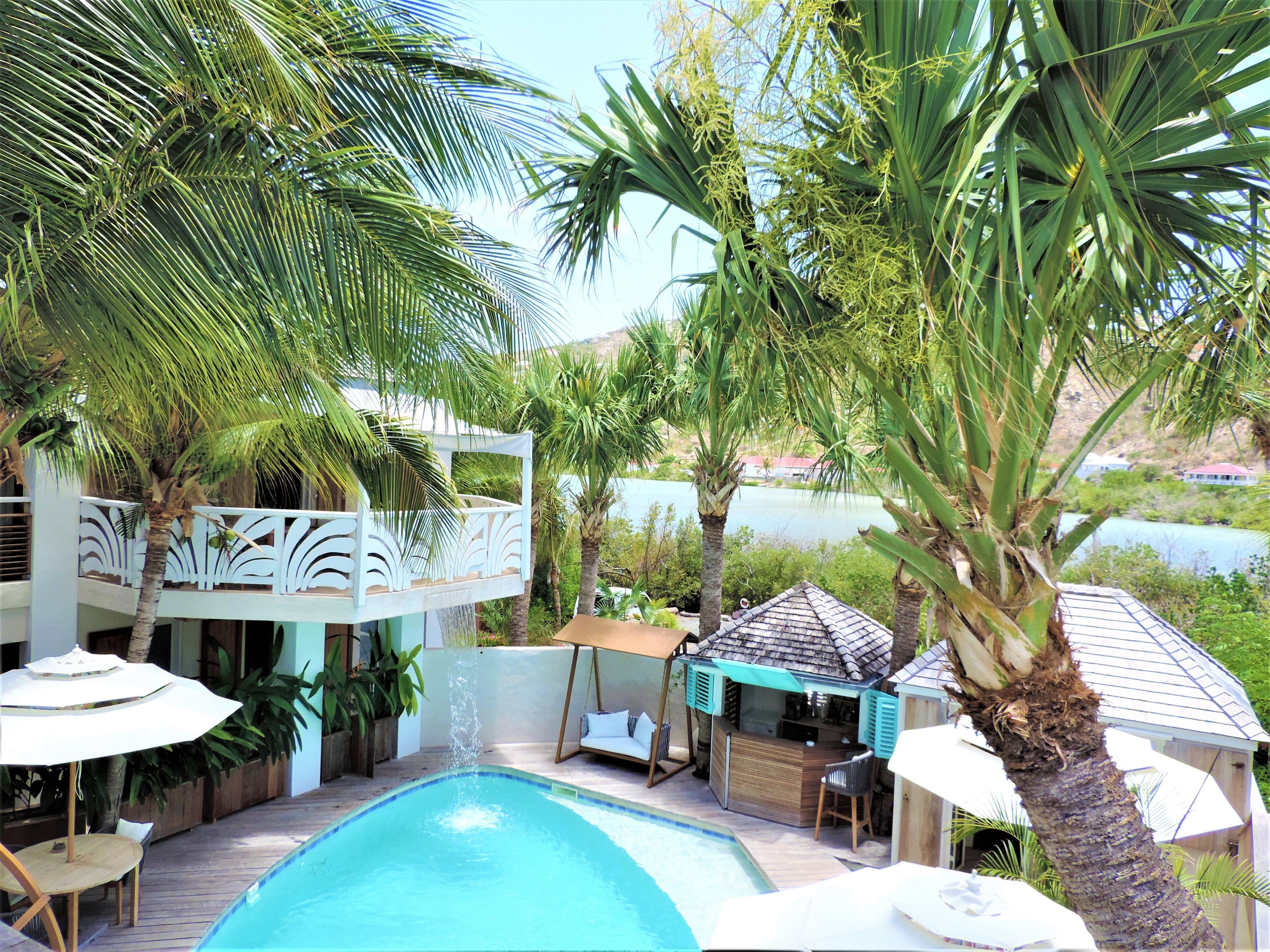 Zona de piscina con bar, asientos al aire libre y palmeras.