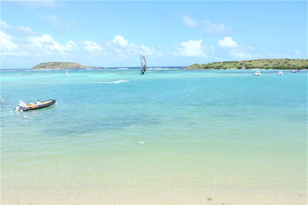 Ein Strand mit klarem türkisblauem Wasser, einem kleinen Boot und einer entfernten Insel.