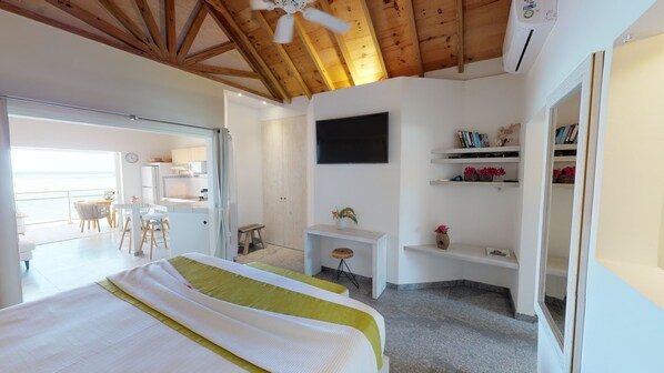 Un dormitorio moderno con una cama grande, un escritorio y un televisor. Cuenta con un balcón con una mesa y sillas.