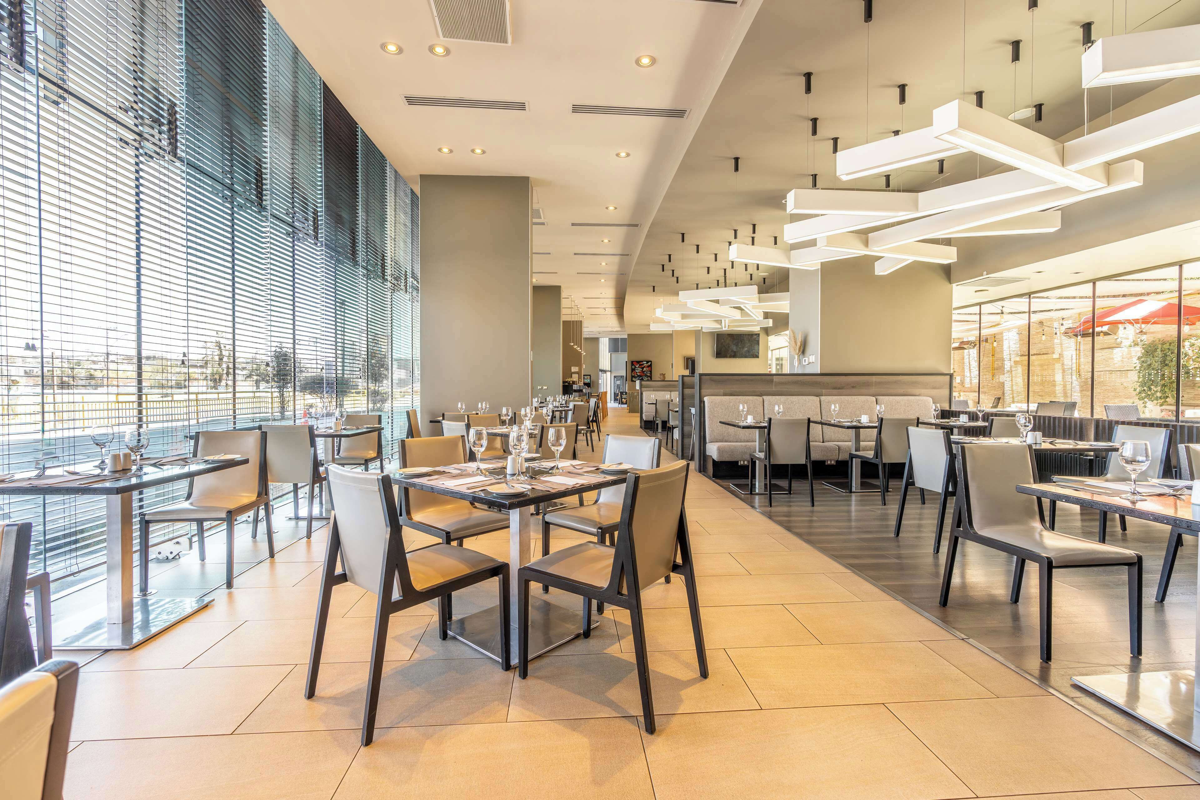 Um restaurante moderno com mesas e cadeiras altas, grandes janelas e luminárias contemporâneas.